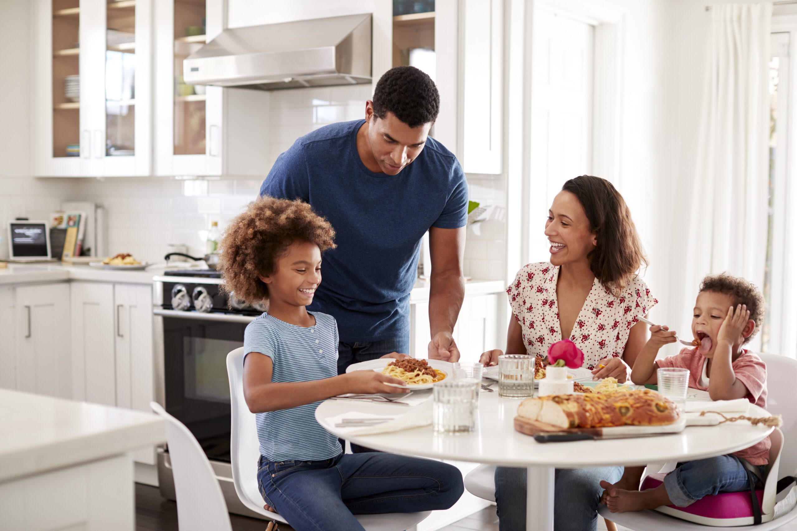 Young mother sitting at table in the kitchen with children, father serving them food, selective focus Young mother sitting at table in the kitchen with children, father serving them food, selective focus